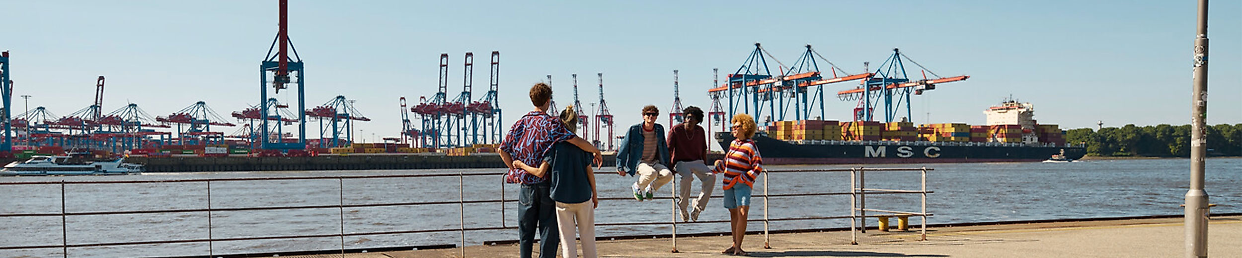 Personengruppe an der Hafenkante mit Blick auf Hafenkräne