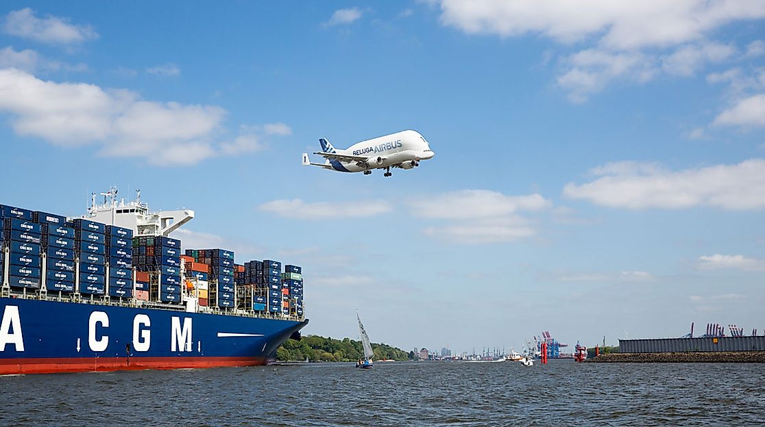 Containerschiff auf der Elbe mit fliegendem Beluga-Frachtflugzeug am Himmel über dem Hamburger Hafen