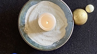 Eine brennende Kerze in einer mit Sand gefüllten Schale und ein Kreuz und Perlen darum herum