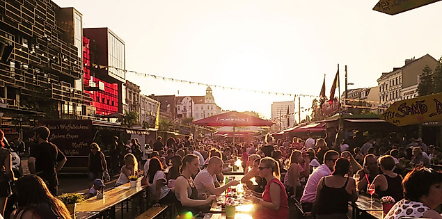 Menschenmenge auf dem Spielbudenplatz in Hamburg bei Sonnenuntergang mit Lichterketten und Festivalatmosphäre.