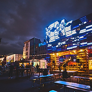 Spielbudenplatz bei Nacht mit beleuchteten Fassaden, Food-Ständen und leuchtender Straßenkunst in Blau und Gelb