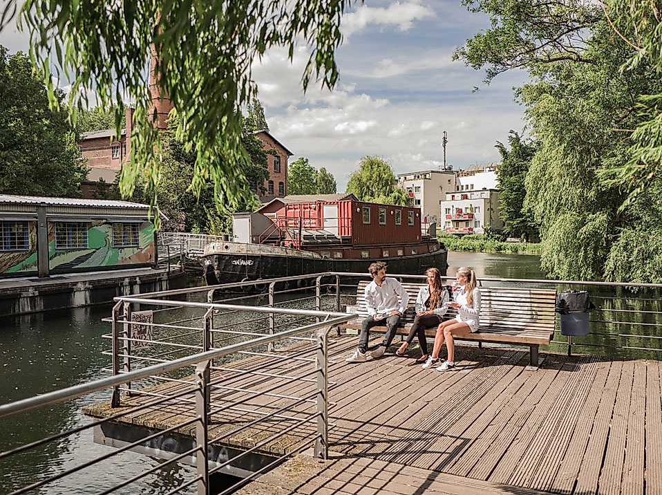 Menschen entspannen an einem Holzsteg am Wasser im alternativen Kultur- und Gartenprojekt Zomia in Wilhelmsburg