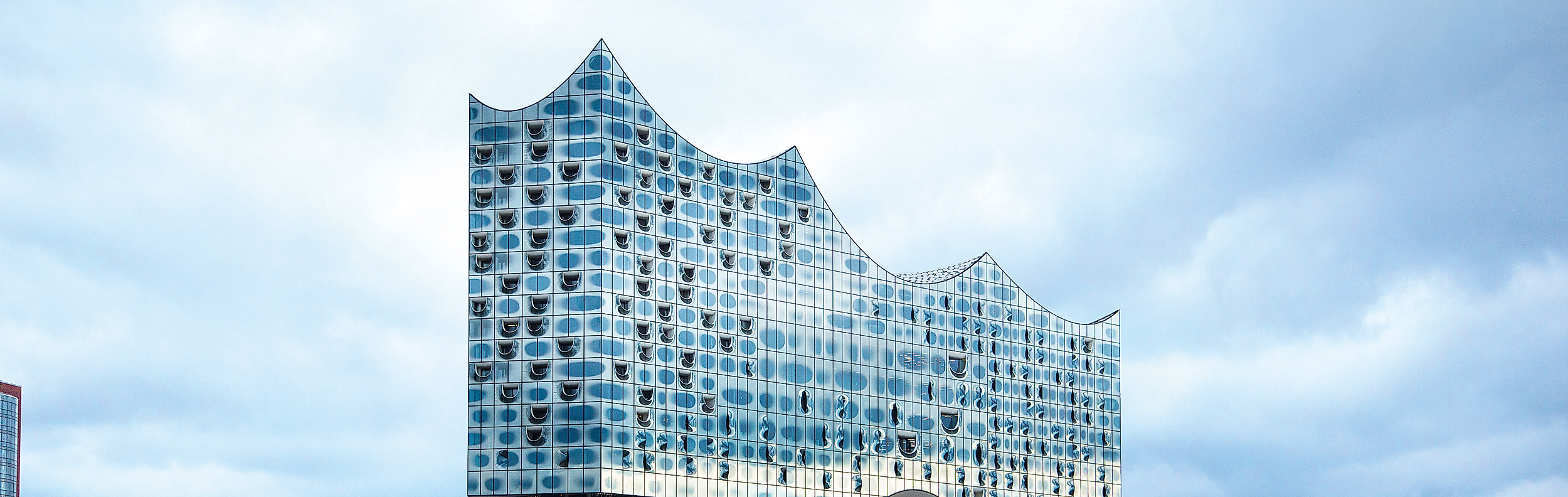 Moderne Glasfassade der Elbphilharmonie in Hamburg mit wolkigem Himmel, Wahrzeichen der Musikstadt.