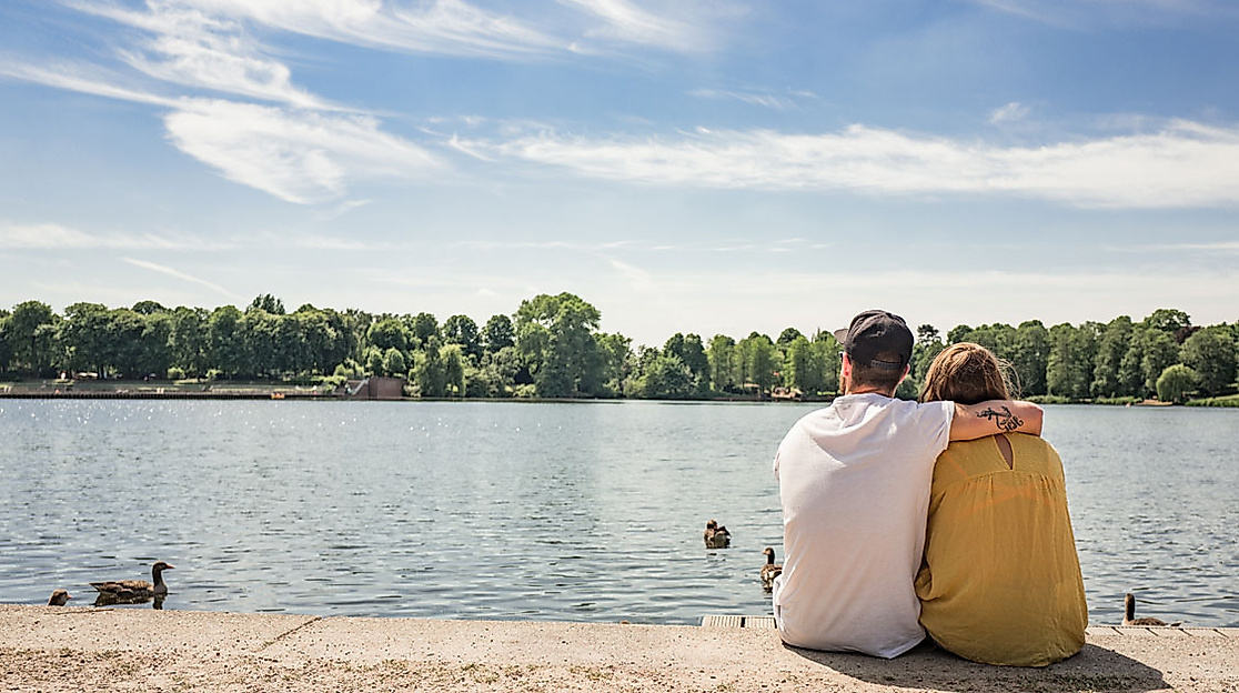 Pärchen sitzt am Ufer des Stadtparksees in Hamburg und blickt aufs Wasser bei sonnigem Wetter