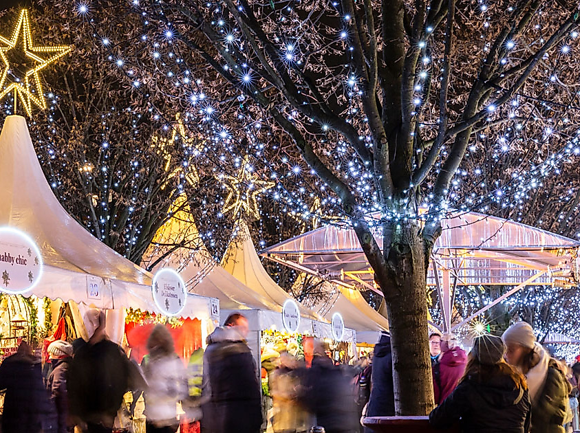 Weihnachtsmarkt in Hamburg mit festlich beleuchteten Zelten und Lichterglanz in den Bäumen bei Nacht.