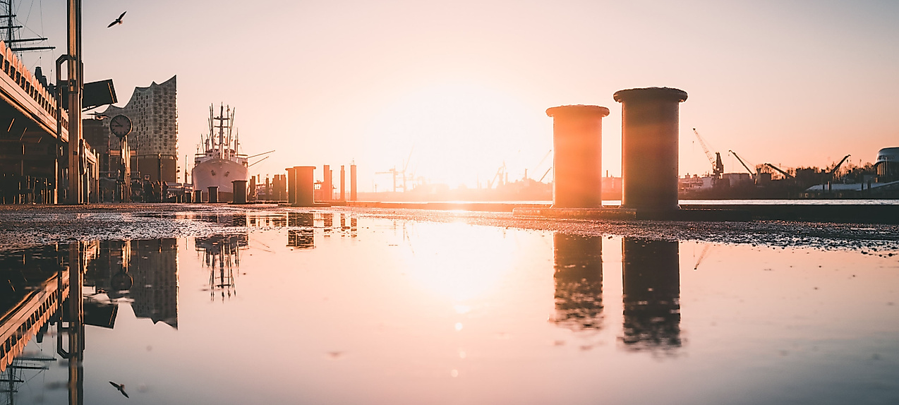 Sonnenaufgang im Hamburger Hafen mit Spiegelung auf nasser Kaimauer und Silhouetten von Kränen und Gebäuden