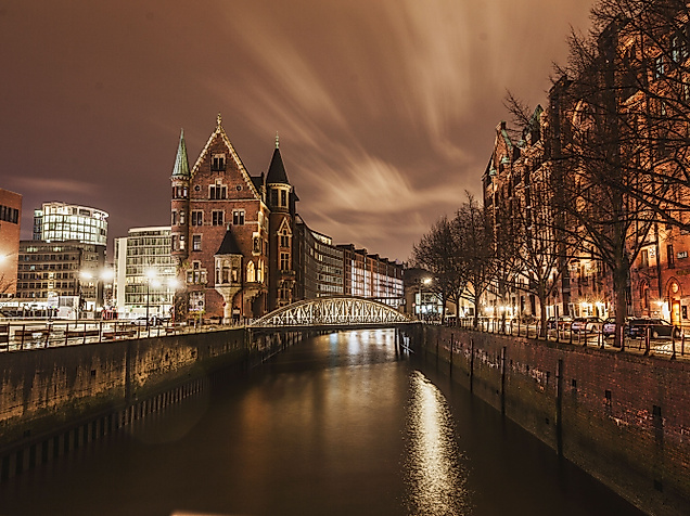 Beleuchtete Speicherstadt bei Nacht mit spiegelndem Wasserlauf und Bäumen am Ufer
