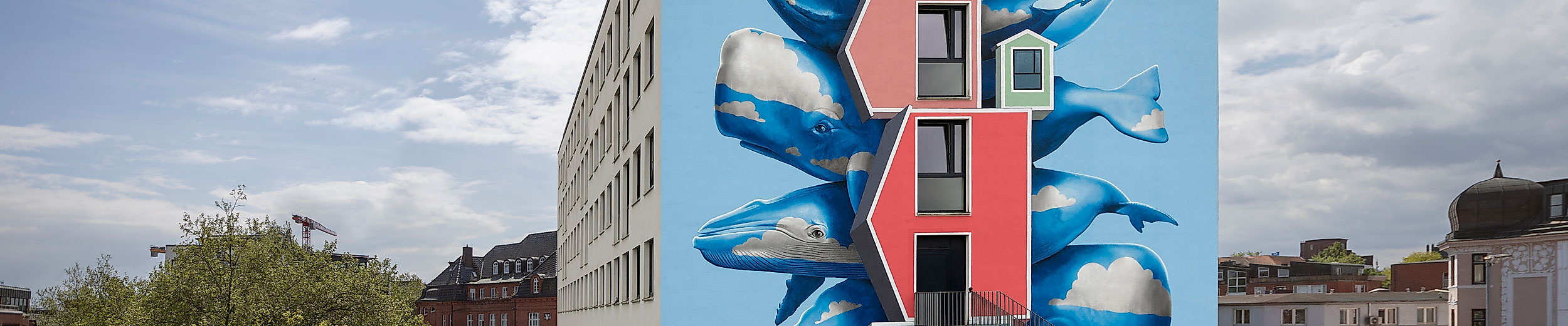 Bunte Hausfassade in Hamburg mit 3D-Wandgemälde fliegender Fische auf blauem Hintergrund bei Sonnenschein