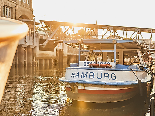 Barkasse mit Hamburg-Schriftzug liegt im Sonnenlicht an den Landungsbrücken im historischen Hafenbecken