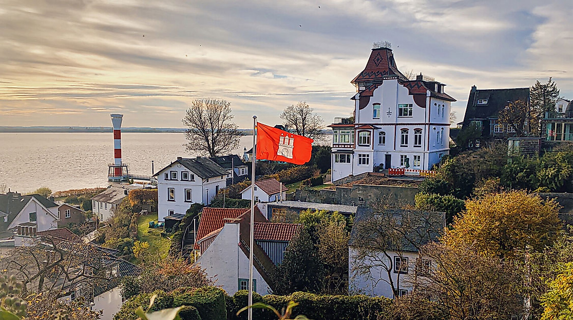 Blick auf das Blankeneser Treppenviertel mit Hamburg-Flagge, historischen Villen und Leuchtturm an der Elbe.
