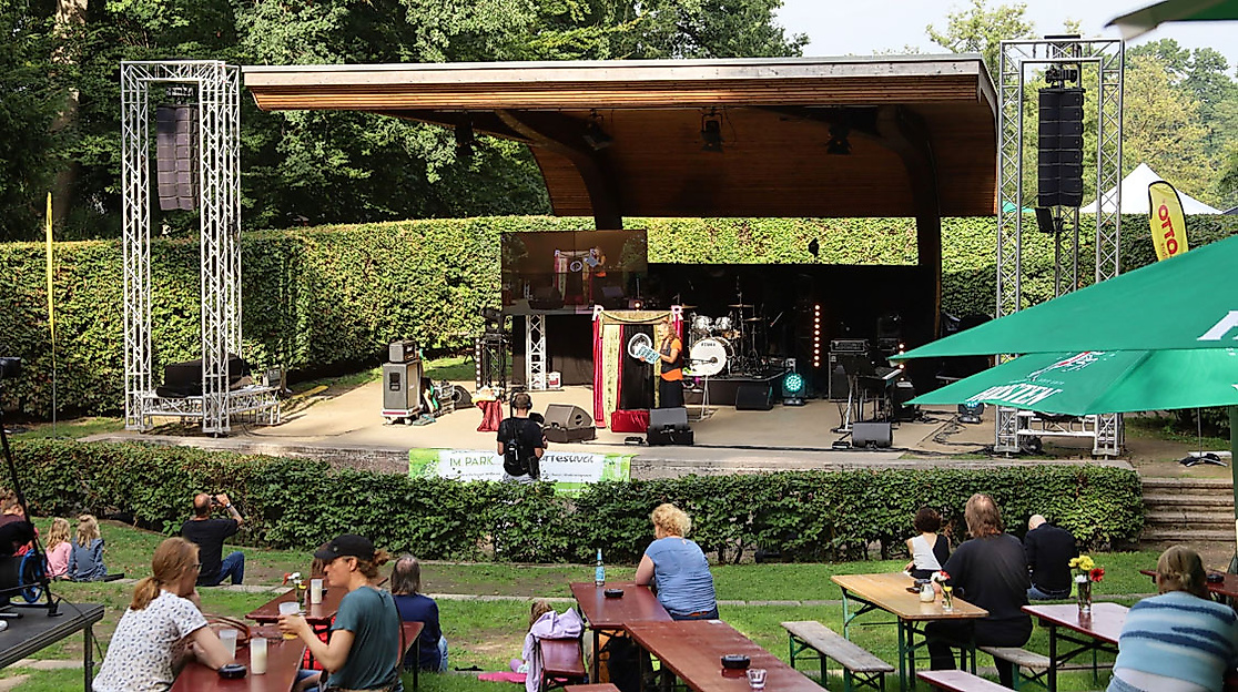 Freiluftbühne mit Livemusik im Park in Hamburg-Harburg, davor Zuschauer:innen auf Bänken bei sonnigem Wetter