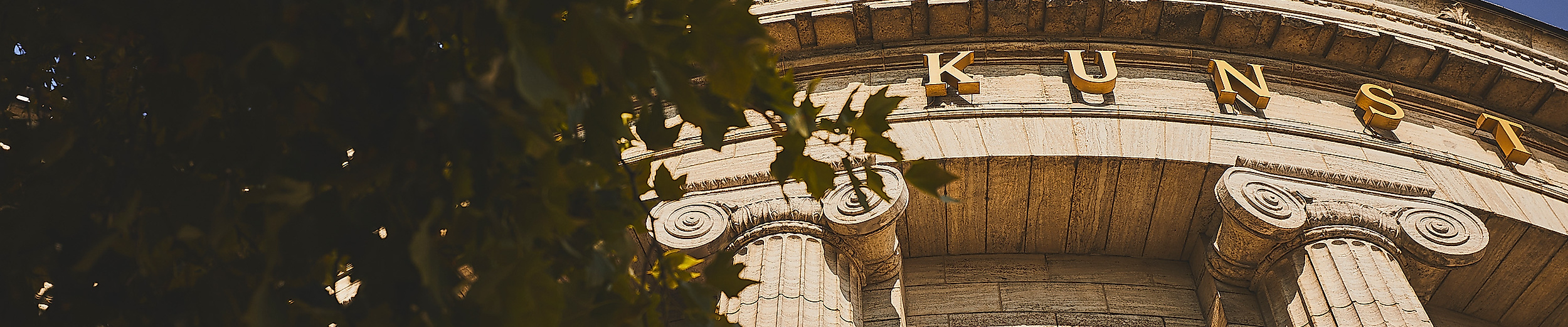 Nahaufnahme der hellen Rundfassade der Hamburgischen Kunsthalle mit Blattwerk im Vordergrund.