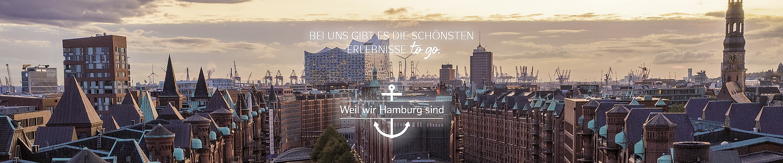 Abendliche Ansicht der Hamburger Speicherstadt mit Elbe, darüber der Text:" BEI UNS GIBT ES DIE SCHÖNSTEN ERLEBNISSE TO GO". Weil wir Hamburg sind. und Hamburg-Wappen.