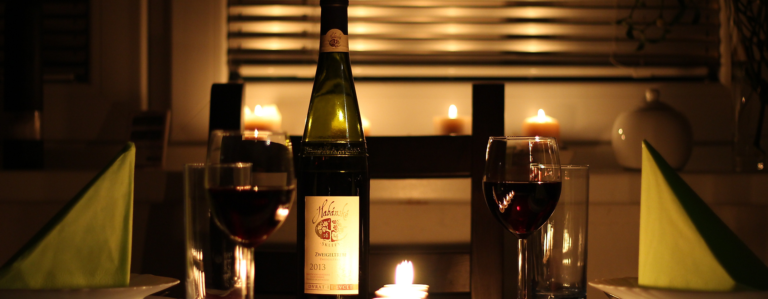 Romantisch gedeckter Tisch mit Kerzenlicht, Rotwein und Weinflasche für ein Candle-Light-Dinner