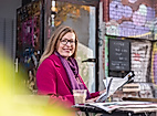 Lächelnde Frau mit Zeitschrift und Getränk im Straßencafé vor bunt besprühter Wand im Hamburger Schanzenviertel.