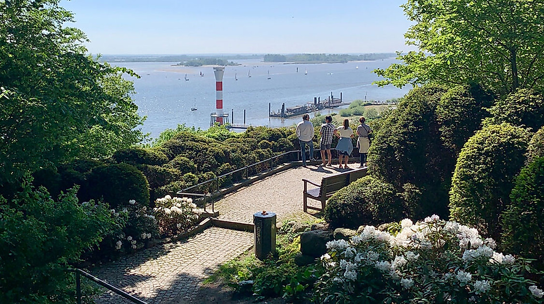 Sitzbereich mit Elbblick inmitten blühender Sträucher und Bäume an einem sonnigen Frühlingstag in Blankenese