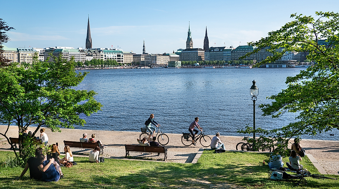 Menschen sitzen und radeln an der sonnigen Binnenalster mit Blick auf Hamburgs historische Stadtsilhouette.