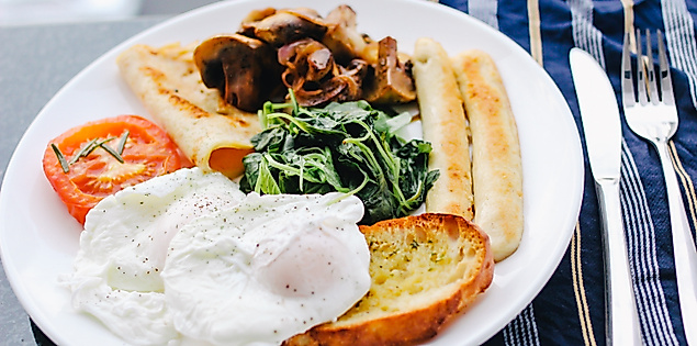 Frühstücksteller mit pochierten Eiern, Spinat, Pilzen, Tomate, Brot und Toast auf weißem Teller