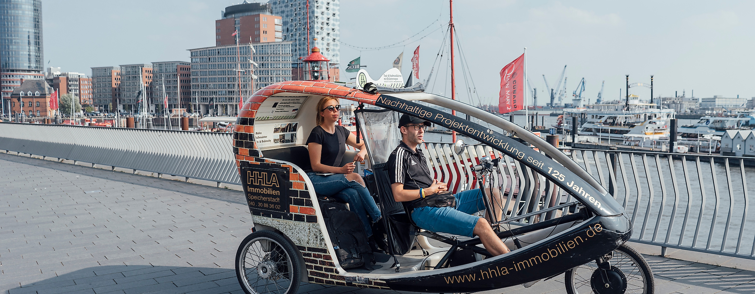 Rikscha mit zwei Fahrgästen an den Landungsbrücken, im Hintergrund die Elbphilharmonie
