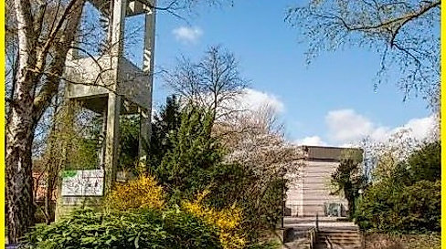Kirchturm mit grünen Sträucher und im Hindergrund Kirchengebäude