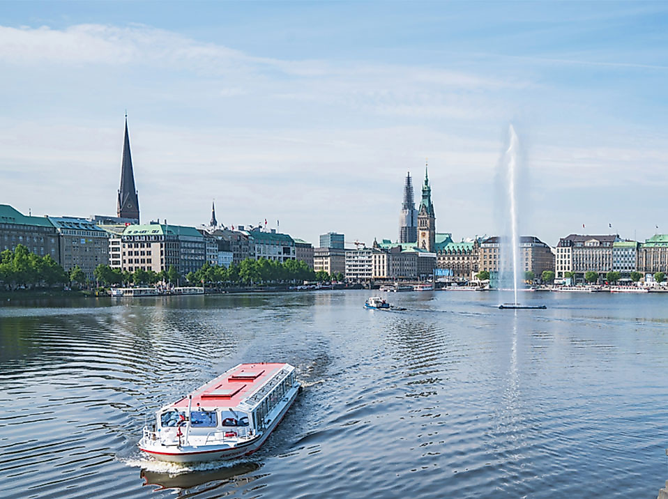 Alsterdampfer auf der Binnenalster in Hamburg mit Wasserfontäne und Kirchtürmen der Altstadt im Hintergrund