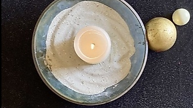 brennende Kerze in einer Sandschale mit Kreuz und Perlen von oben