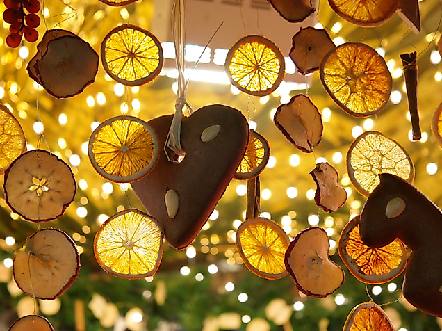 Weihnachtsdeko aus Orangenscheiben und Holzanhängern vor Lichterglanz am Tannenbaum