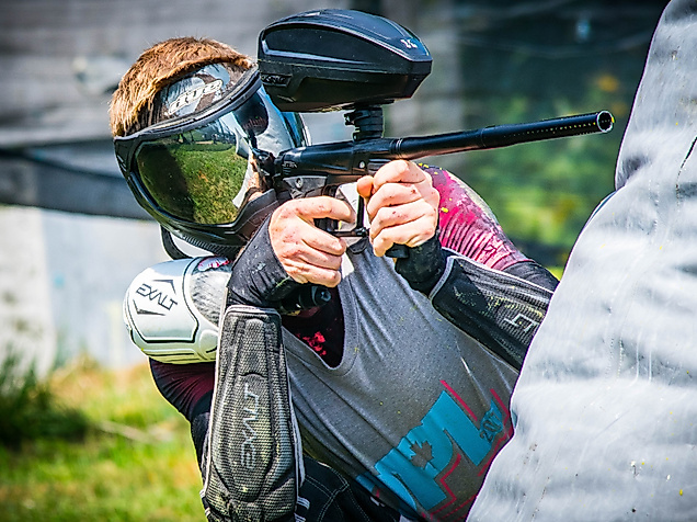 Paintball-Spieler mit Schutzmaske und Markierer zielt konzentriert hinter einer Deckung im Spielfeld