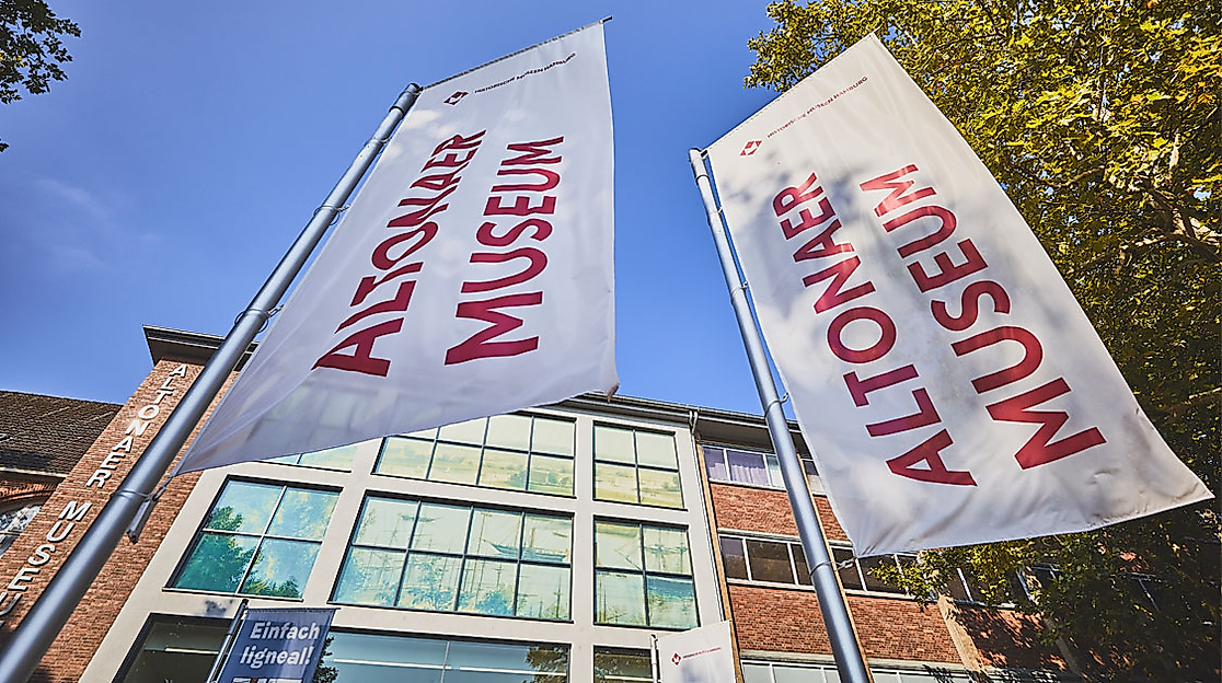 Fahnen mit Aufschrift „Altonaer Museum“ vor dem Museumsgebäude in Hamburg an einem sonnigen Tag