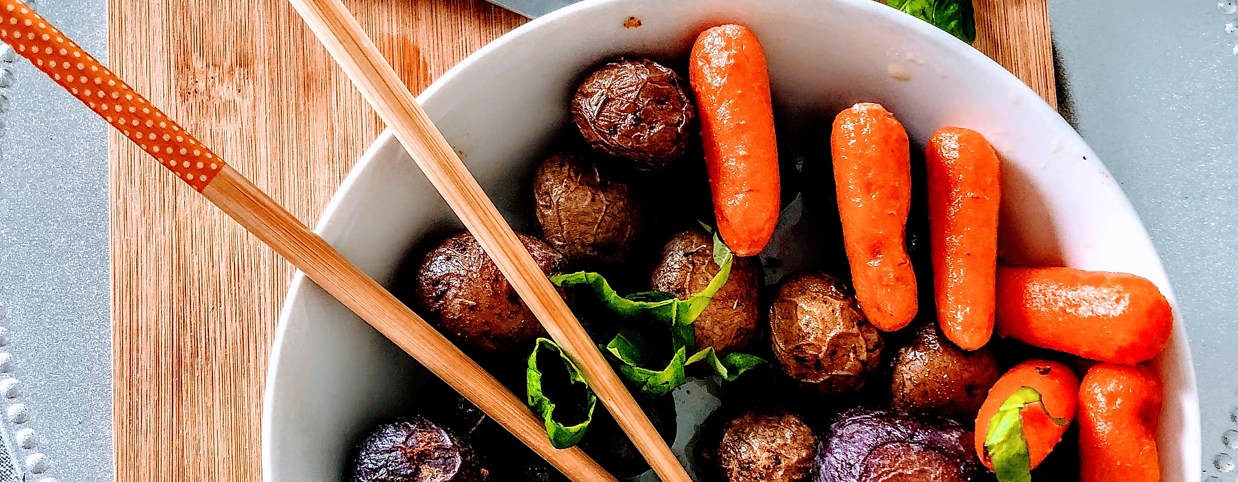 Bunte vegane Bowl mit Gemüse, Falafel und Sesam, serviert auf Holzbrett mit Essstäbchen und Zitrone