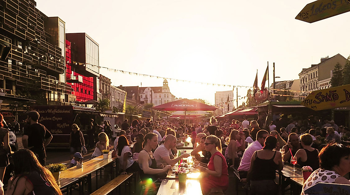 Menschenmenge auf dem Spielbudenplatz in Hamburg bei Sonnenuntergang mit Lichterketten und Festivalatmosphäre.