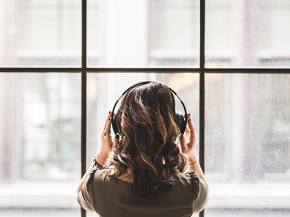 Frau mit Kopfhörern blickt aus dem Fenster, Symbolbild für die Podcast-Vielfalt von Hamburg Tourismus.