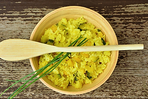 Schüssel mit gelbem Curryreis, garniert mit Schnittlauch, dazu Holzlöffel auf rustikalem Holztisch