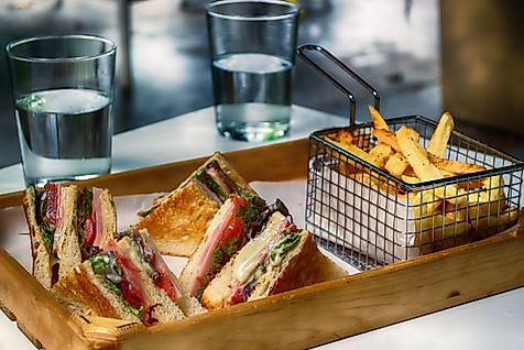 Toast-Sandwiches mit Pommes in Metallkörbchen auf Holztablett, dazu zwei Gläser Wasser.
