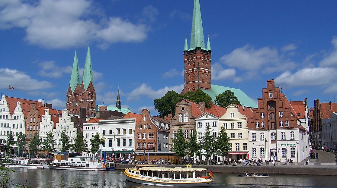 Altstadt von Lübeck mit historischen Giebelhäusern und Kirchtürmen am Wasser bei Sonnenschein