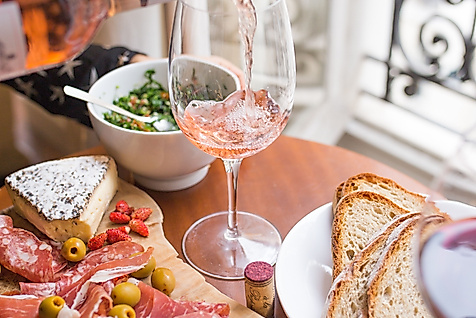 Französische Charcuterie-Platte mit Schinken, Käse, Oliven und Baguette, dazu Roséwein am Fenster.