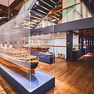 Ausstellungsraum im Internationalen Maritimen Museum mit beleuchtetem Schiffsmodell in Glasvitrine.