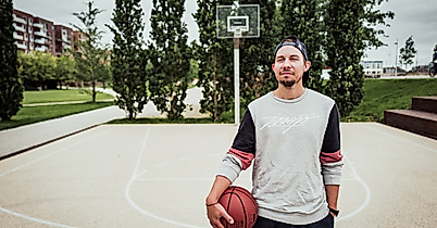 Junger Mann mit Basketball steht auf dem Sportfeld im Lohsepark vor einem Korb und hohen Bäumen