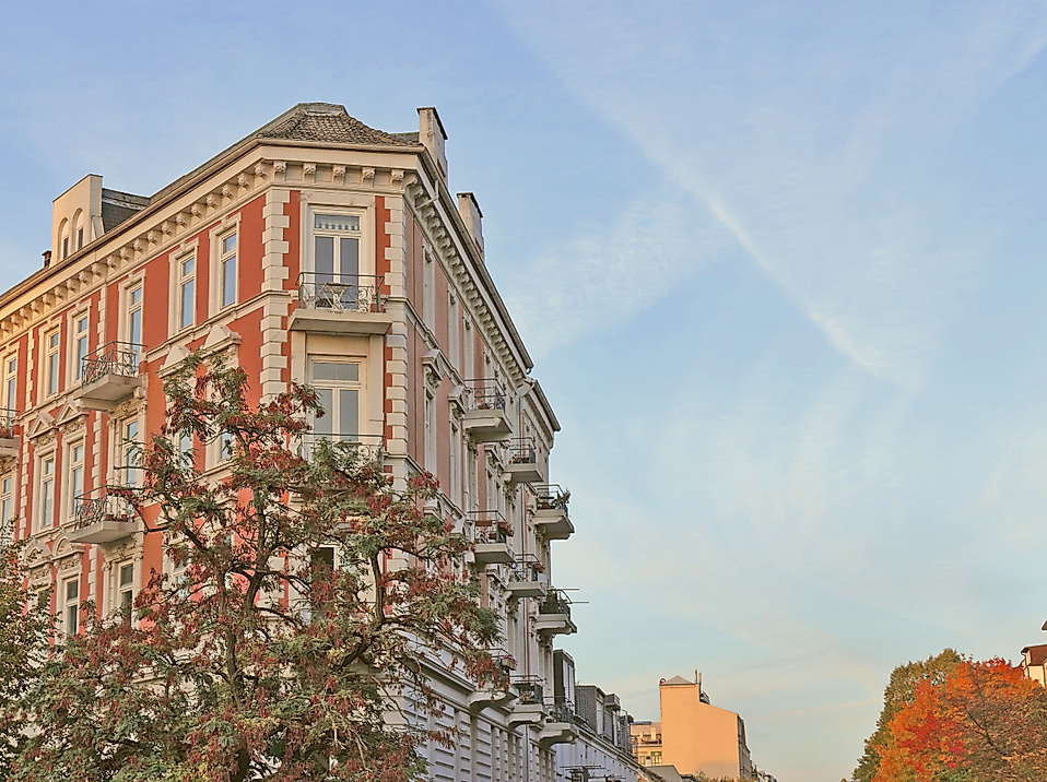 Gründerzeitfassade in Hamburg-Eppendorf im Abendlicht vor herbstlich gefärbten Bäumen und blauem Himmel