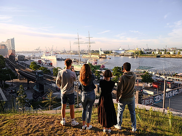 Vier Freunde schauen auf den Hamburger Hafen bei Sonnenaufgang