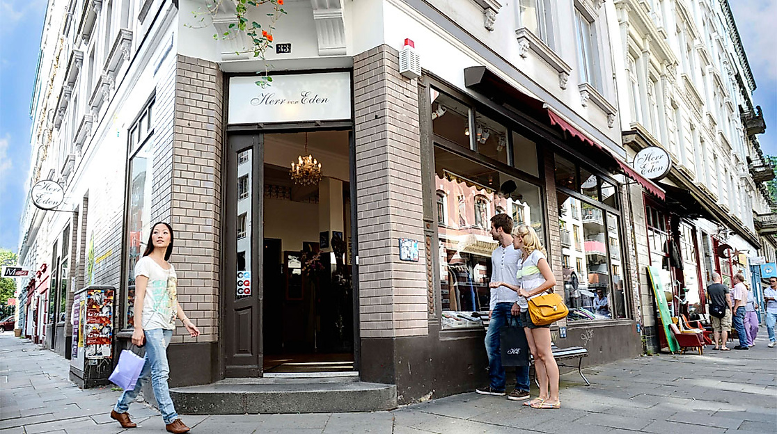 Menschen flanieren und shoppen an einer belebten Straßenecke mit Boutiquen im Karoviertel