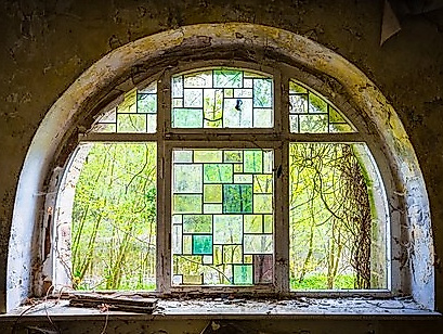 Blick aus einem Rundbogenfenster, mit Bleikristalleinfassungen im Grünton, in die Natur