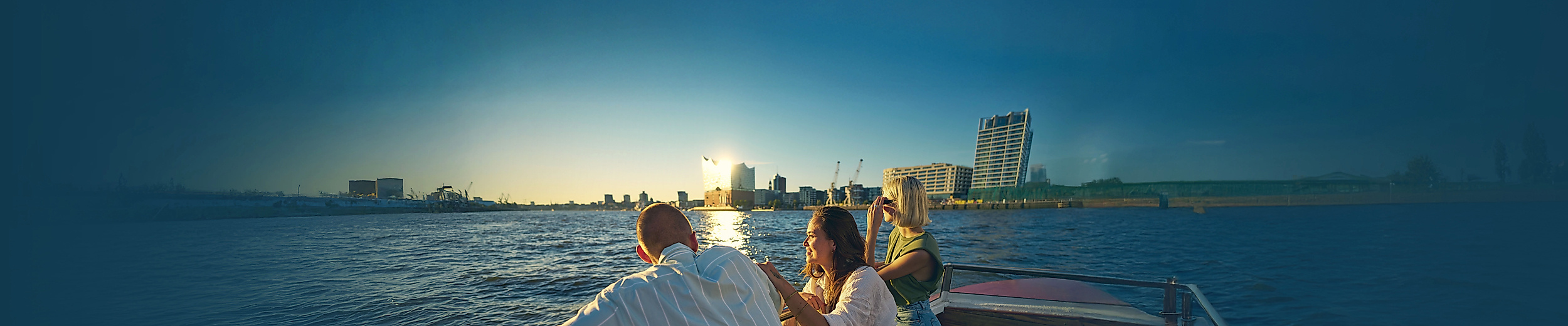 Drei junge Personen auf einer Barkasse im Sommer mit Elbphilharmonie im Hintergrund