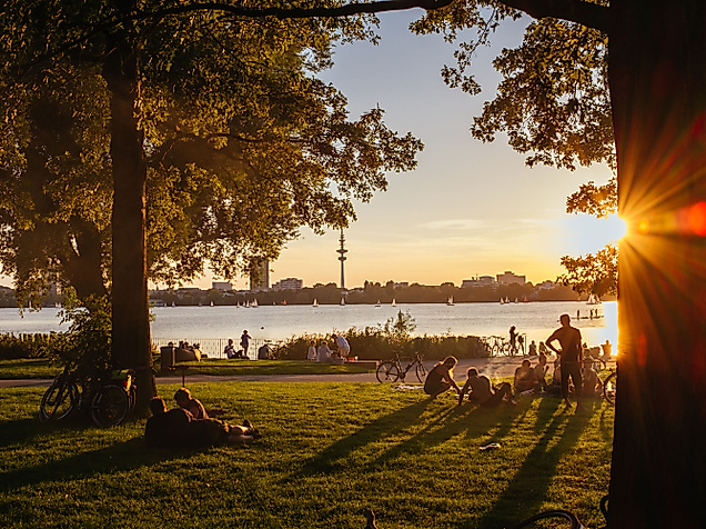 Sonnenuntergang im Alsterpark mit Blick durch Bäume auf entspannte Menschen an der Außenalster