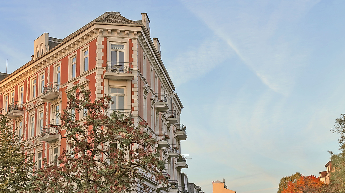 Gründerzeitfassade in Hamburg-Eppendorf im Abendlicht vor herbstlich gefärbten Bäumen und blauem Himmel