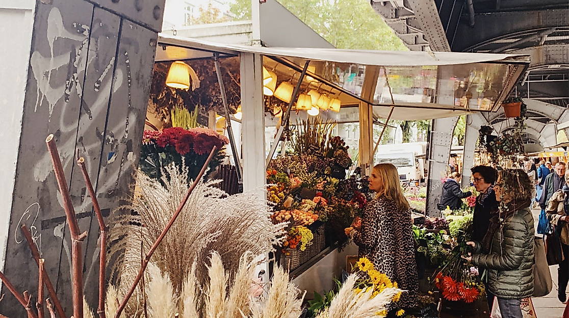 Blumenstand auf dem Isemarkt in Hamburg mit herbstlicher Dekoration und Marktbesucher:innen unter der U-Bahn-Trasse