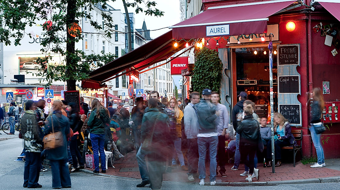 Menschen vor Bar mit roter Markise im Szeneviertel Ottensen, lebendige Abendstimmung auf der Straße