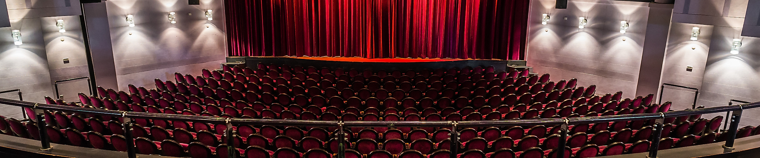 Blick in den Theatersaal des Winterhuder Fährhauses mit roten Sitzreihen und geschlossener Bühne