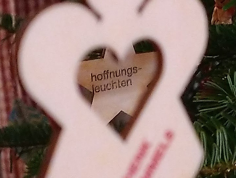 Durch einen Holzengel mit einem Herzausschnitt erkennt man einen Holzstern mit der Aufschrift "hoffnungsleuchten"