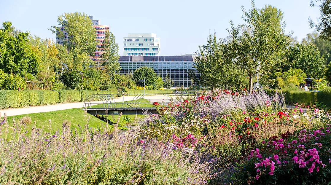 Blühende Beete und Spazierwege im Inselpark Wilhelmsburg mit dem Gebäude der Umweltbehörde im Hintergrund